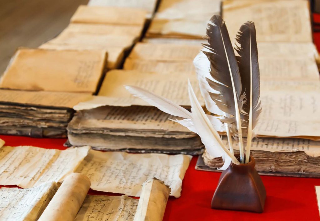 feathers and inkpot with Old books on the red tablecloth